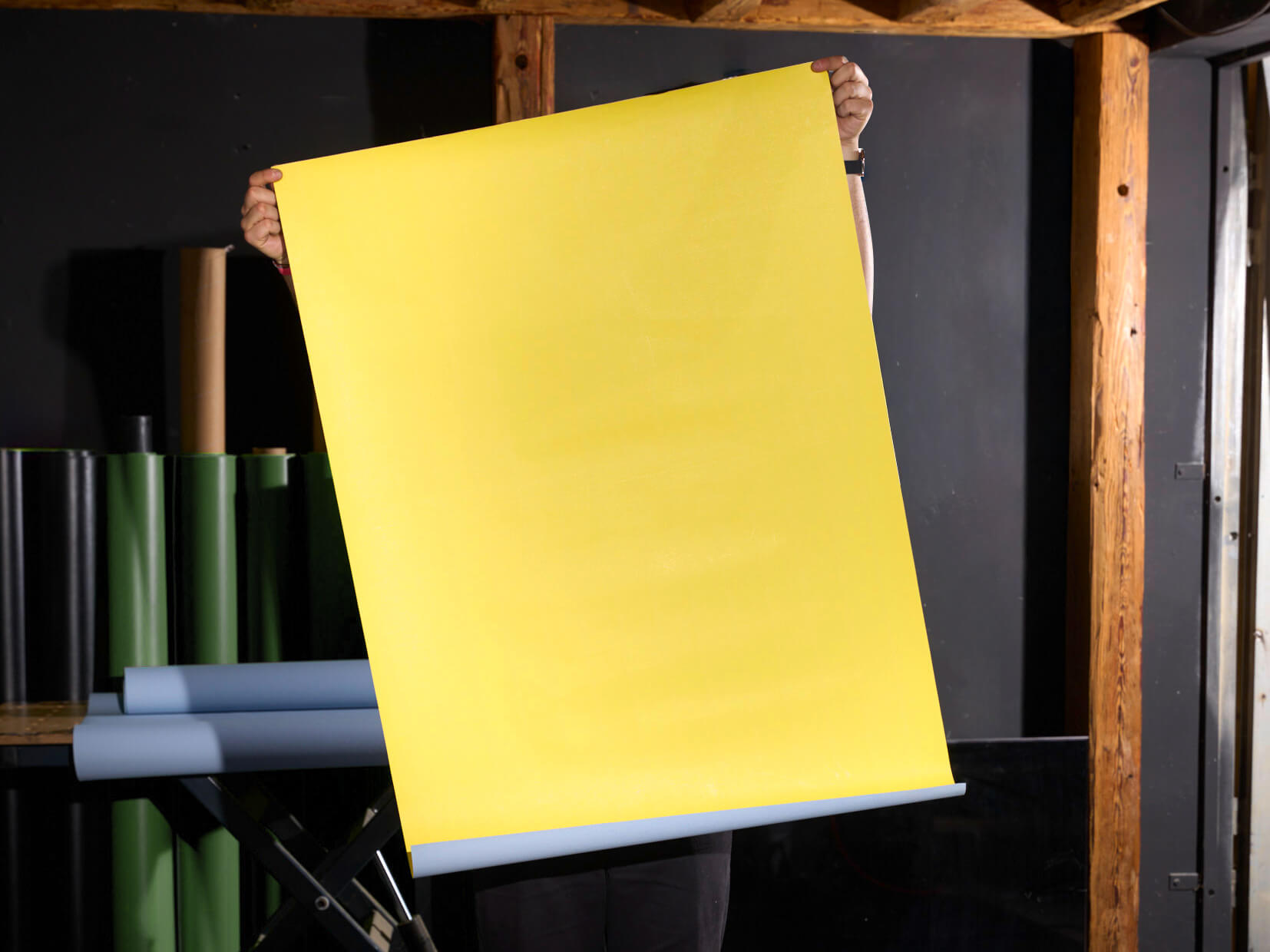 Ein übergroßes gelbes Blatt Papier wird in einem Raum mit Stühlen und Tischen in der Luft gehalten.