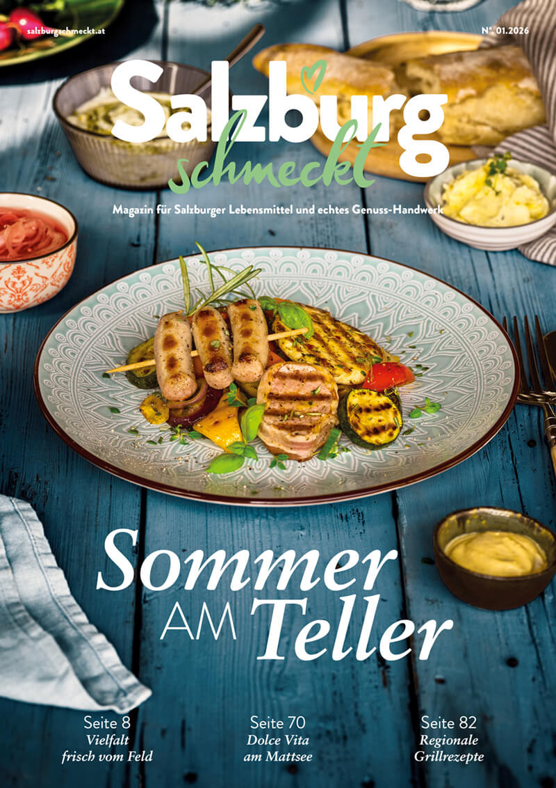Ein Teller mit einer Portion Spätzle, garniert mit Röstzwiebeln und Petersilie, dazu eine Gabel und ein Glas Wasser. Im Hintergrund ein Schild mit dem Namen "Sommers Am Teller" und dem Gericht "Salzbung".